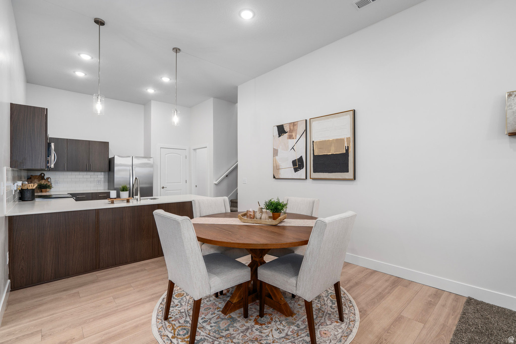 Dining area with light wood finished floors, a high ceiling, and recessed lighting