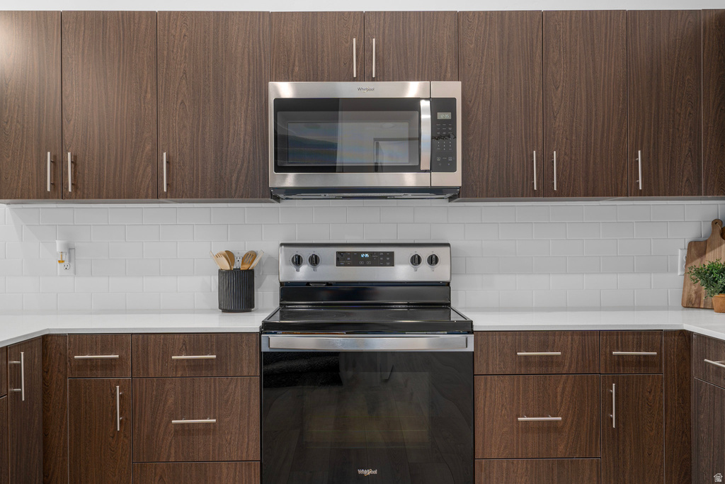 Kitchen featuring stainless steel appliances, tasteful backsplash, dark wood finish cabinets, and modern cabinets
