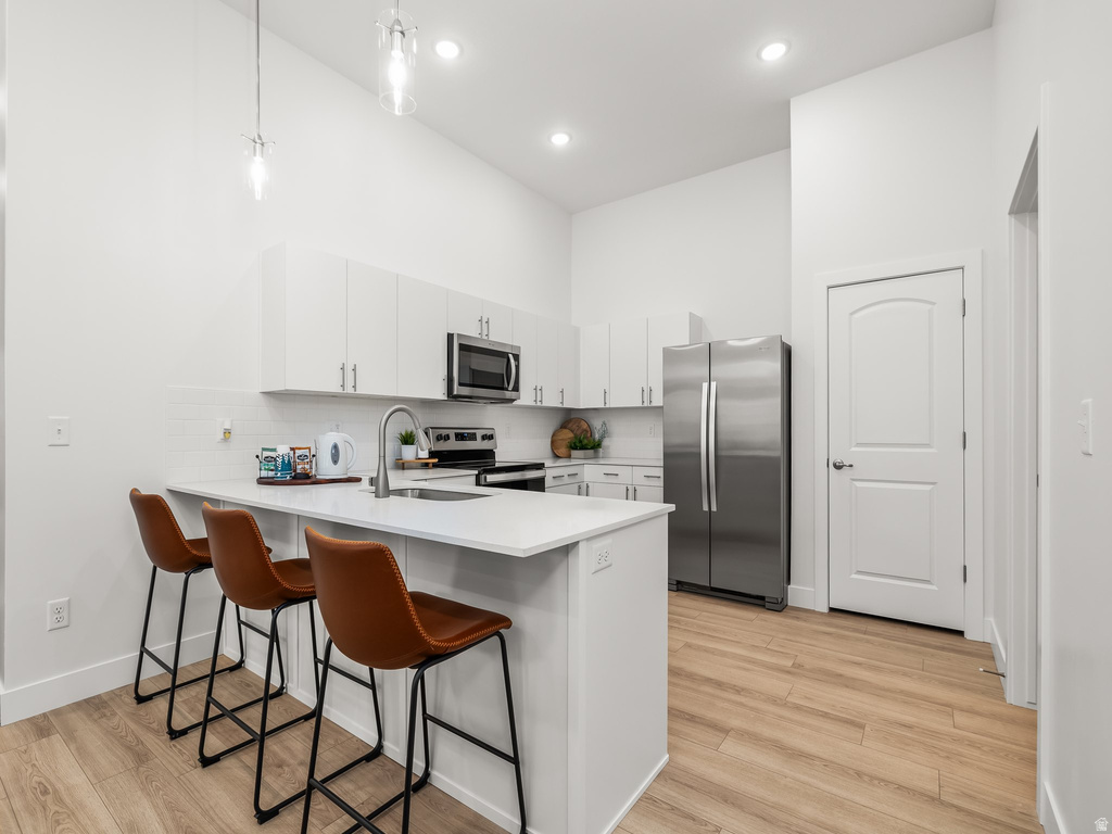 Kitchen featuring a breakfast bar area, a high ceiling, stainless steel appliances, white cabinetry, and a peninsula