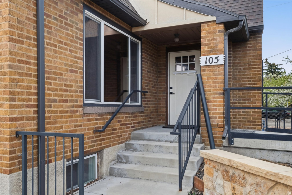 Doorway to property with brick siding and roof with shingles