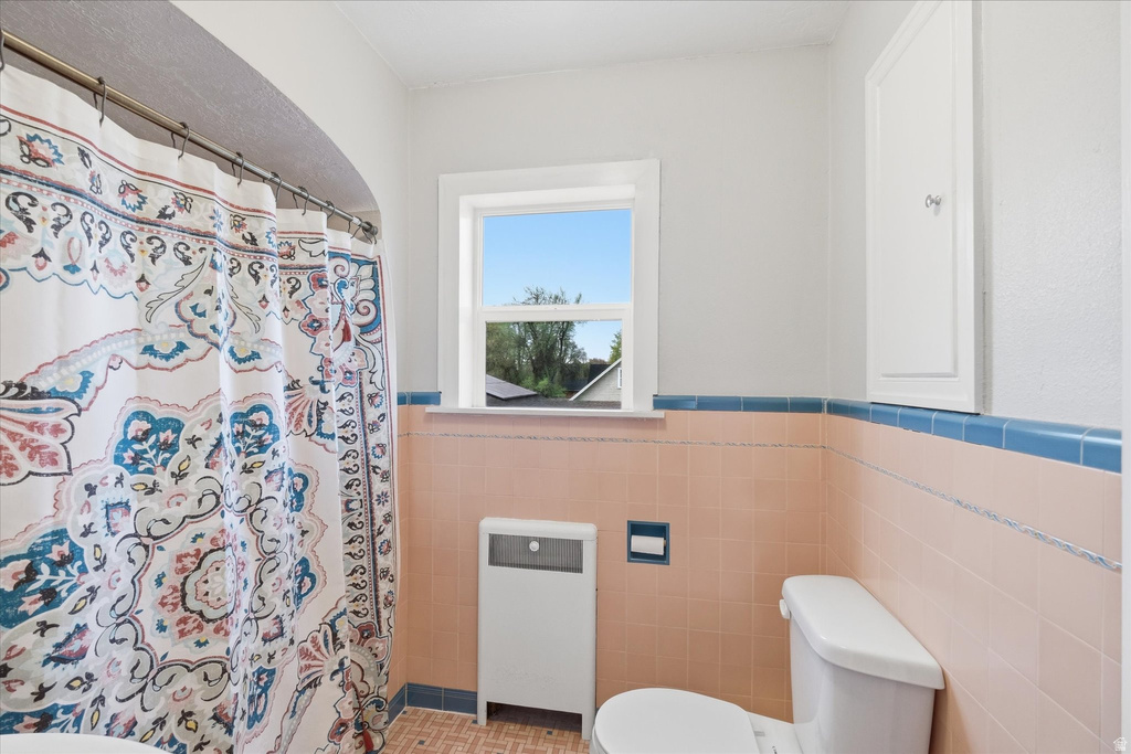 Bathroom with a shower with curtain, a wainscoted wall, heating unit, and tile walls