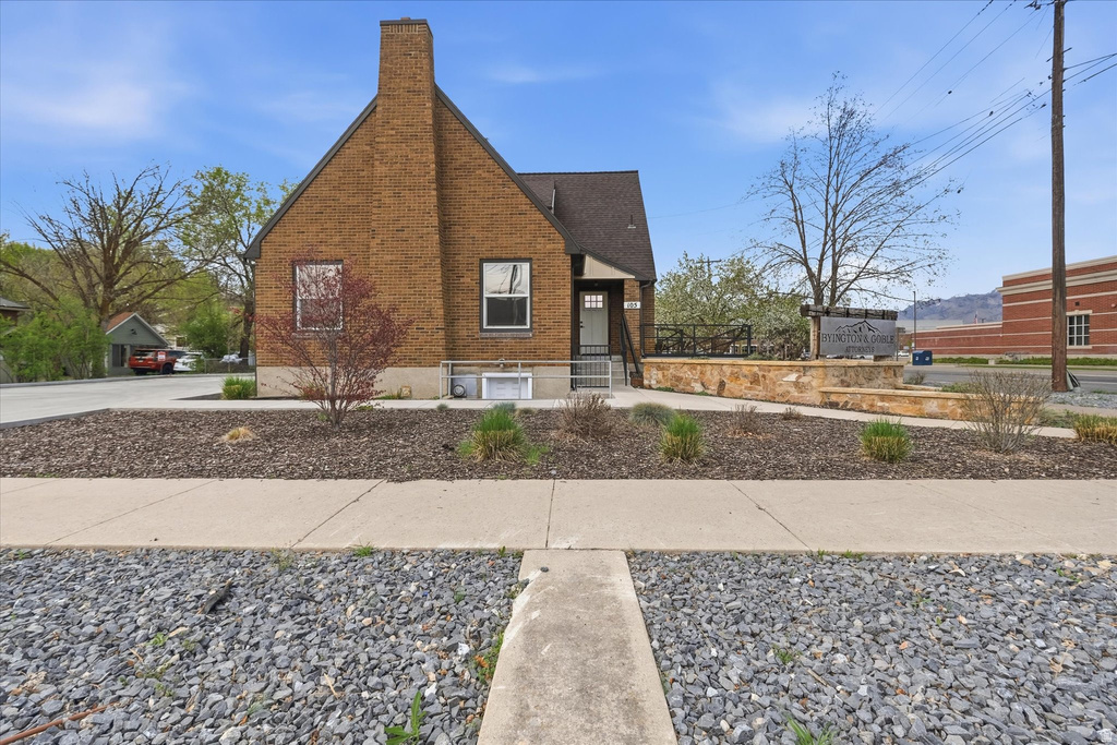 View of side of property with brick siding, a chimney, and a shingled roof