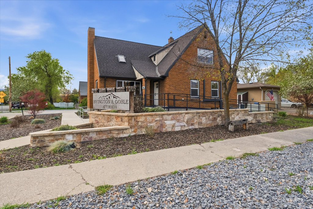 View of front of property featuring brick siding, a chimney, and roof with shingles