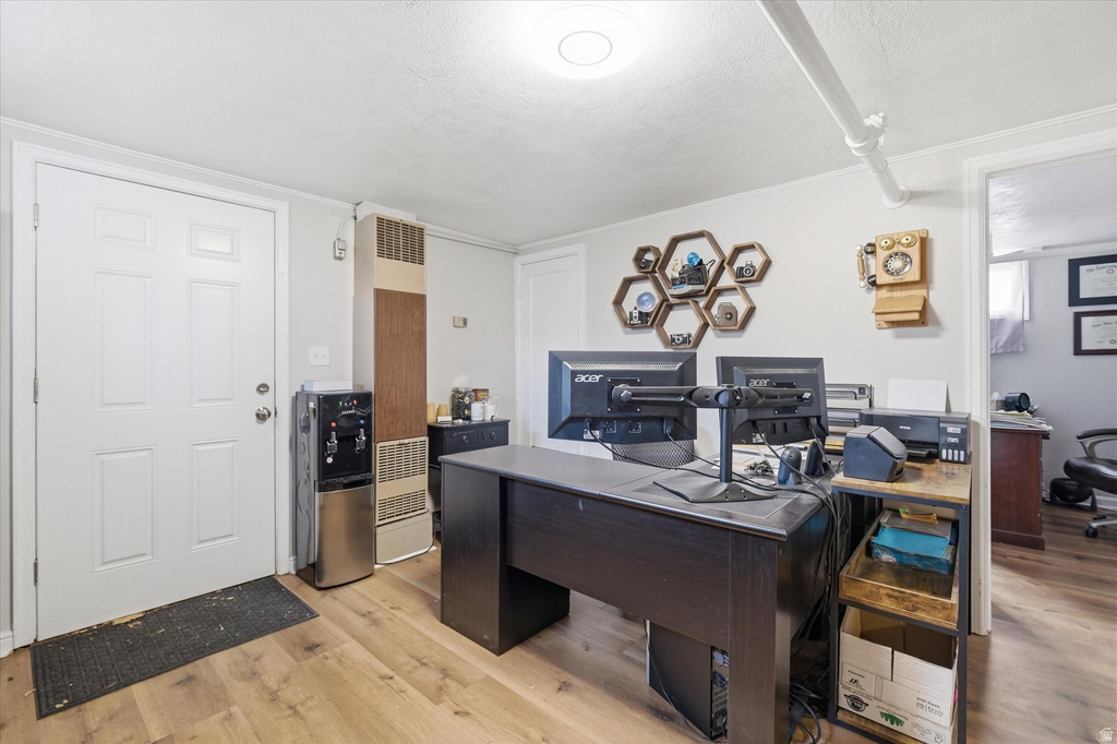 Home office with light wood-type flooring, a heating unit, and a textured ceiling