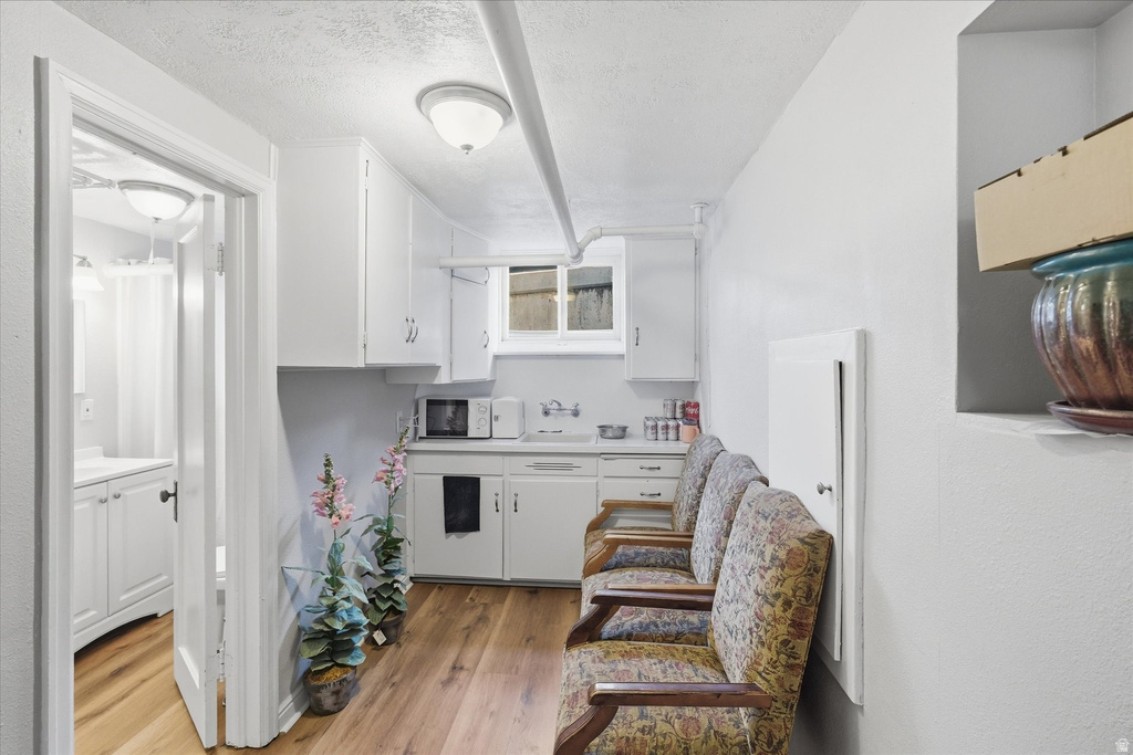 Kitchen with light countertops, white cabinets, light wood-style flooring, a textured ceiling, and white microwave