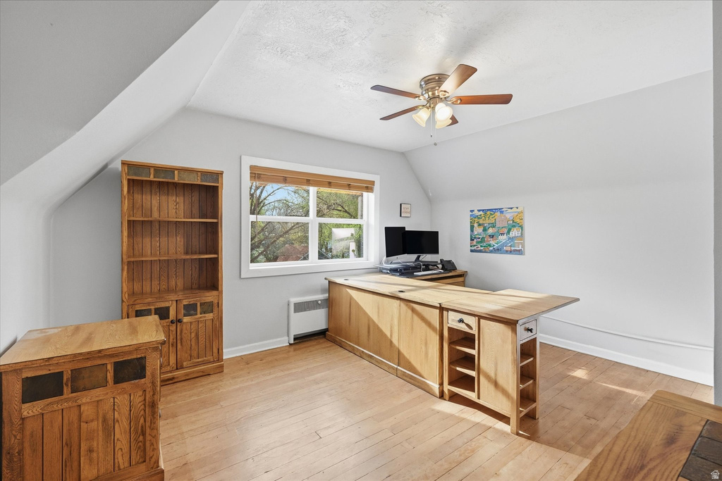 Office space featuring lofted ceiling, light wood-style floors, radiator heating unit, and a ceiling fan