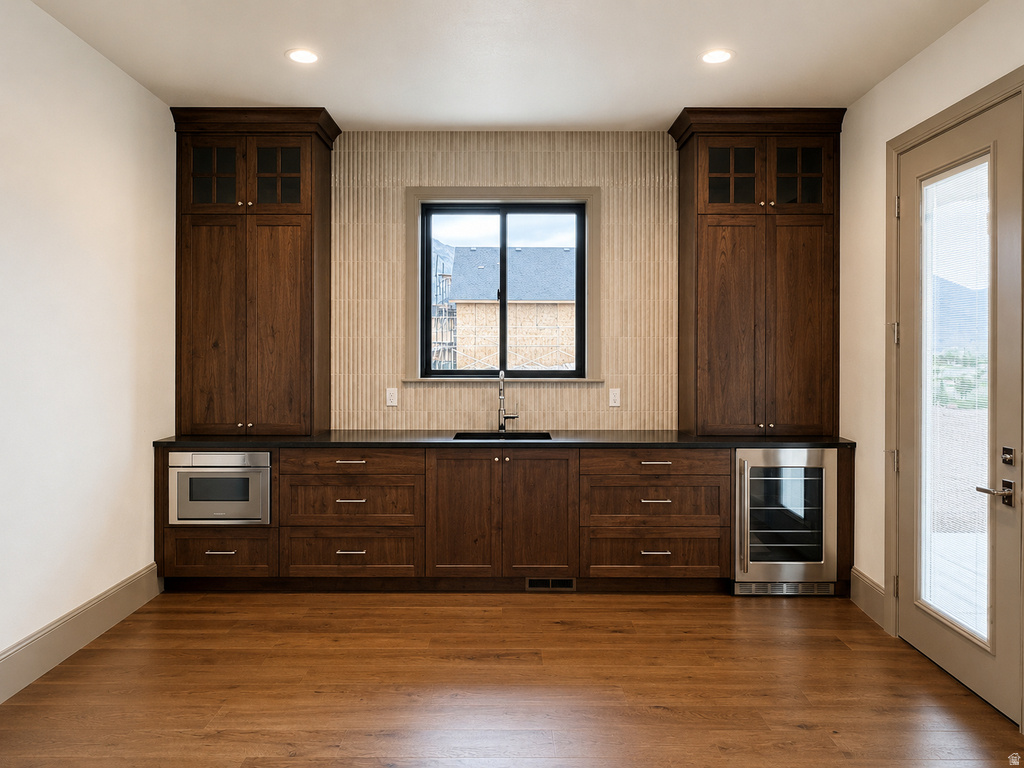 Built-in cabinetry with glass-front uppers, dark countertop, undermount sink, and wood-finish flooring