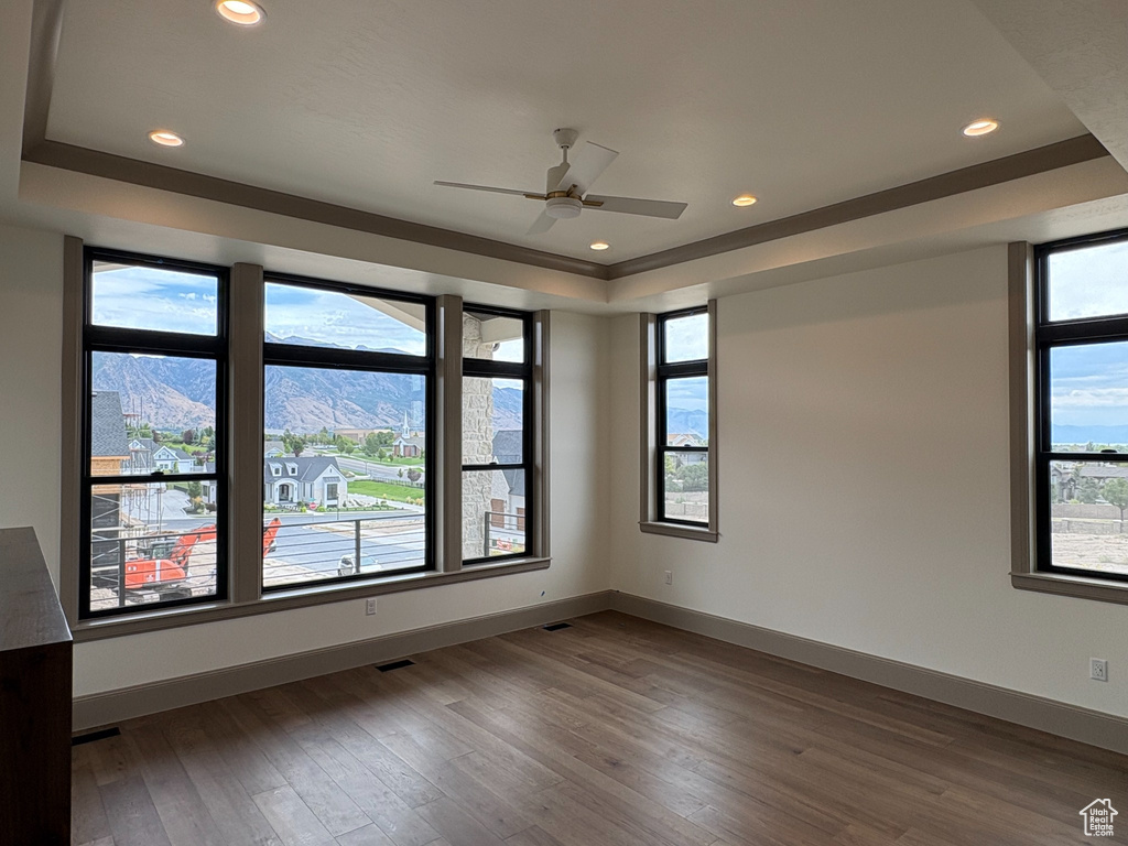 Expansive windows, tray ceiling with recessed lighting, ceiling fan, wood-finish flooring, and neutral wall tones