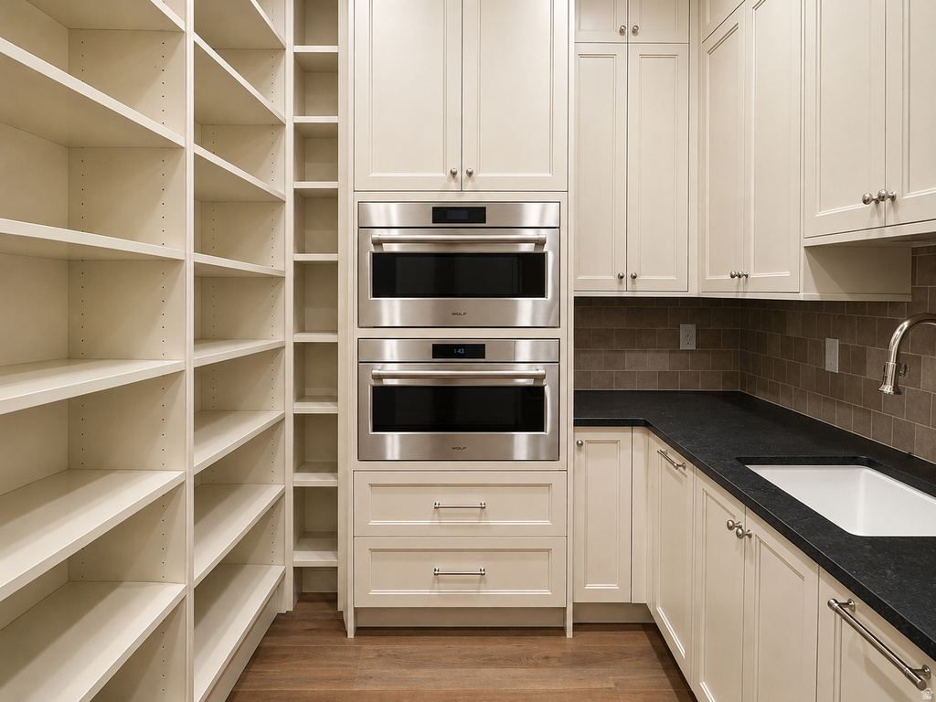 Extensive built-in shelving, stacked stainless steel microwave ovens, cream-colored cabinetry, dark countertops, and a subway tile backsplash