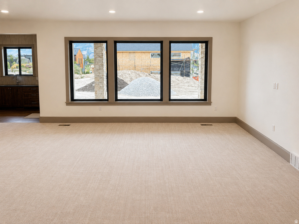 Recessed lighting, large black-framed windows, light beige carpeting, dark baseboards, and white walls
