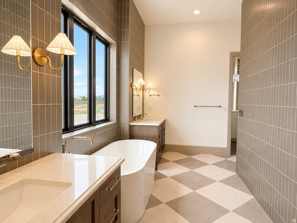 Freestanding soaking tub, dual vanities with integrated sinks, floor-to-ceiling tiled walls, checkerboard tile flooring, and large window with dark trim