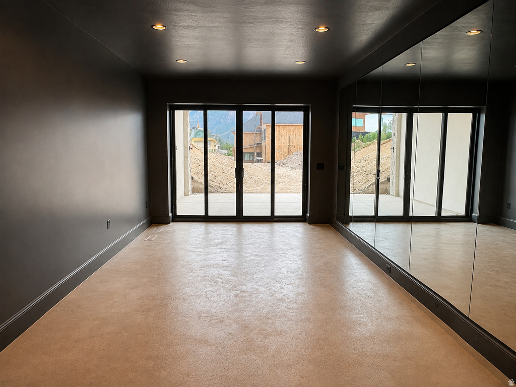 Recessed lighting illuminates an expansive room featuring a full-length mirrored wall and light-toned flooring