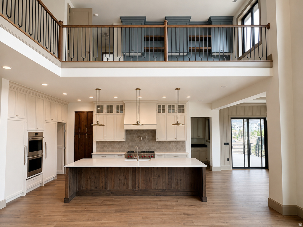 Open-concept kitchen featuring an oversized island with countertop seating, stainless steel double oven, wood-finish flooring, and white cabinetry