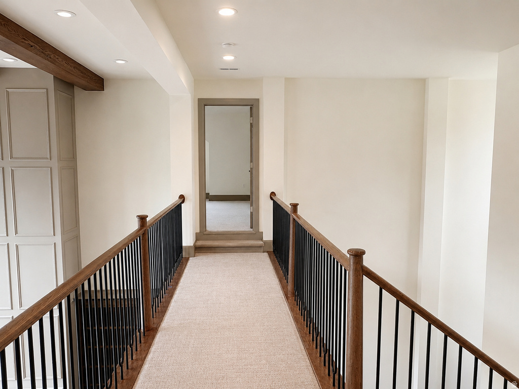 Upper landing featuring a wood-finish handrail with black spindles, recessed lighting, and a neutral carpet runner