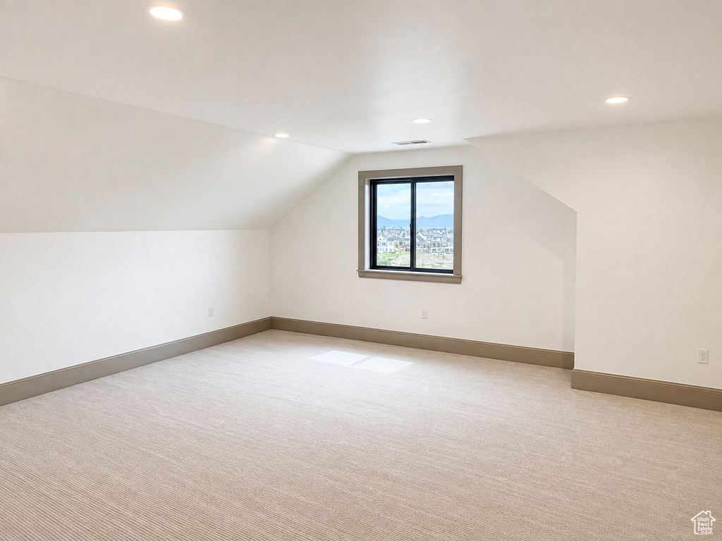 Spacious room featuring sloped ceilings, recessed lighting, a window with a dark frame, and light-toned carpeting