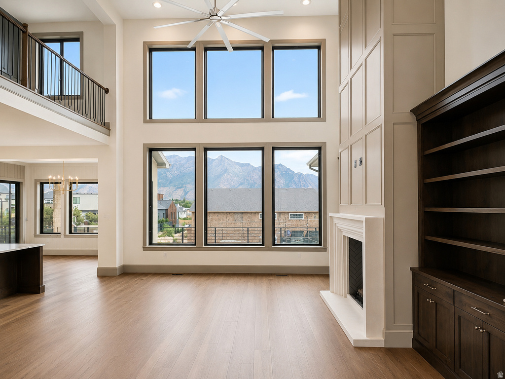 Two-story living area with wood-finish flooring, a contemporary ceiling fan, and a fireplace with a white mantel and paneling