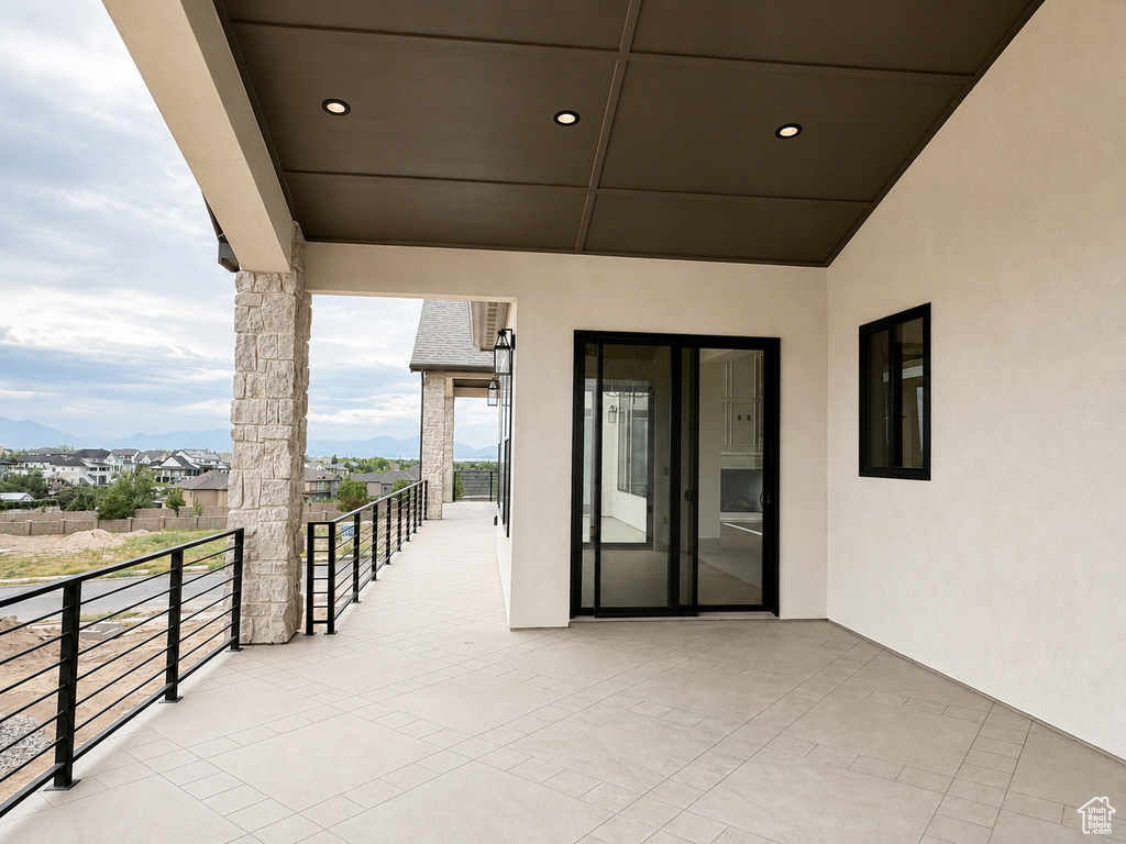 Expansive covered balcony featuring stone-clad pillars, black metal railings, recessed lighting, and large sliding glass doors