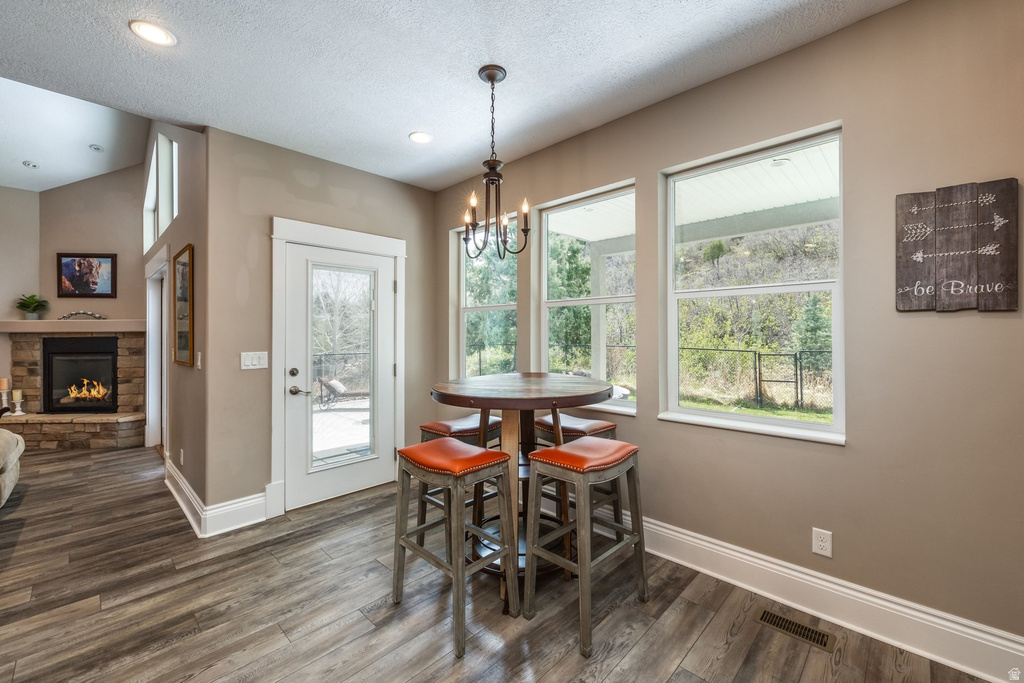 Dining area with a stone fireplace, a textured ceiling, dark wood finished floors, and hanging lights