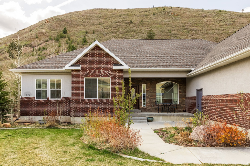 View of front of house with a porch, a front yard, stucco siding, and roof with shingles