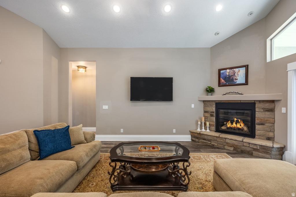 Living room with wood finished floors, a stone fireplace, and vaulted ceiling
