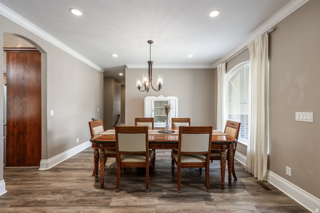 Dining room with arched walkways, dark wood finished floors, ornamental molding, and a chandelier