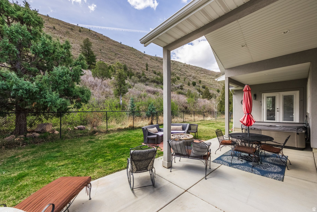 Fenced backyard featuring a patio, a mountain view, a hot tub, french doors, and an outdoor living space with a fire pit