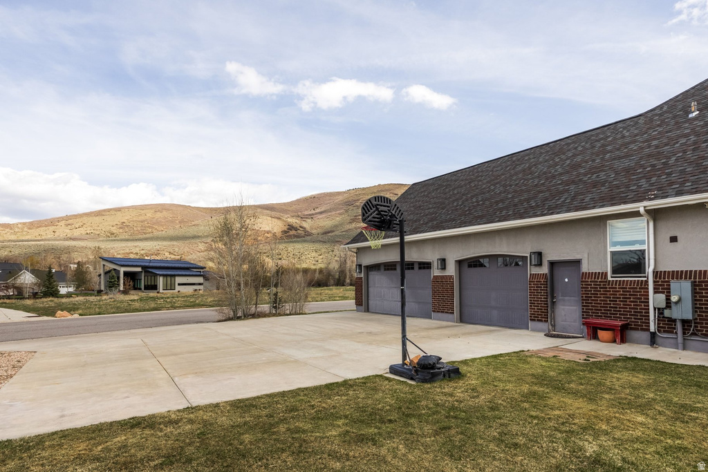View of side of property featuring brick siding, a mountain view, concrete driveway, a lawn, and a garage