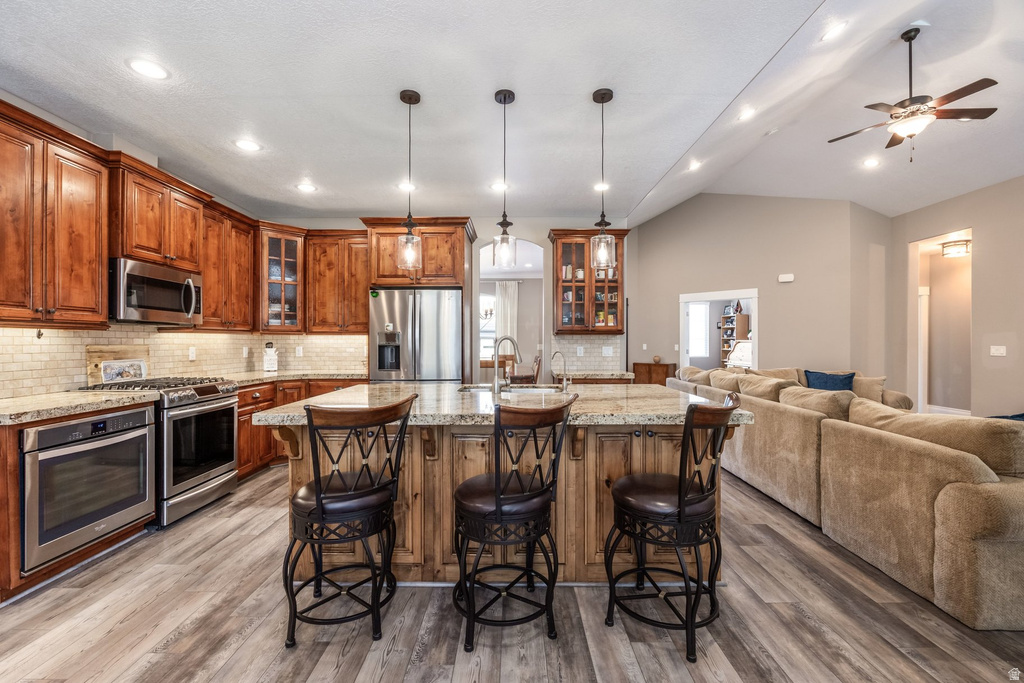 Kitchen with wood finish cabinets, glass insert cabinets, open floor plan, an island with sink, and stainless steel appliances
