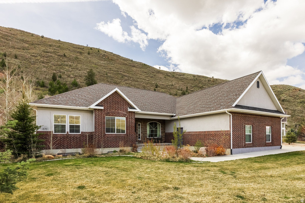 Ranch-style house with brick siding, a front yard, covered porch, stucco siding, and roof with shingles