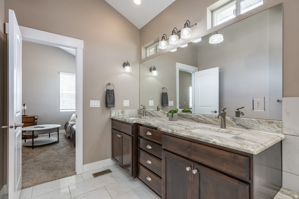 Ensuite bathroom featuring plenty of natural light, double vanity, light marble finish floors, and lofted ceiling