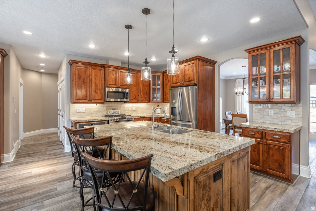 Kitchen featuring wood finish cabinetry, glass insert cabinets, arched walkways, stainless steel appliances, and pendant lighting