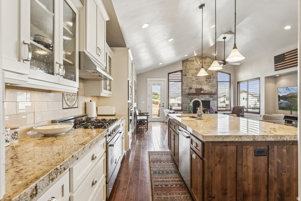 Kitchen featuring stainless steel appliances, lofted ceiling, glass insert cabinets, light stone countertops, and dark wood-style flooring
