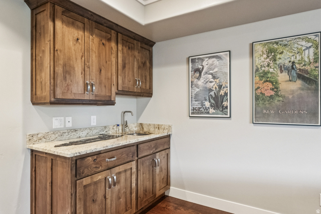 Bar featuring light stone counters and dark wood-type flooring