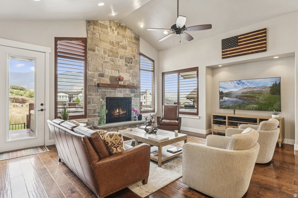 Living room featuring dark wood finished floors, a ceiling fan, a fireplace, plenty of natural light, and a high ceiling