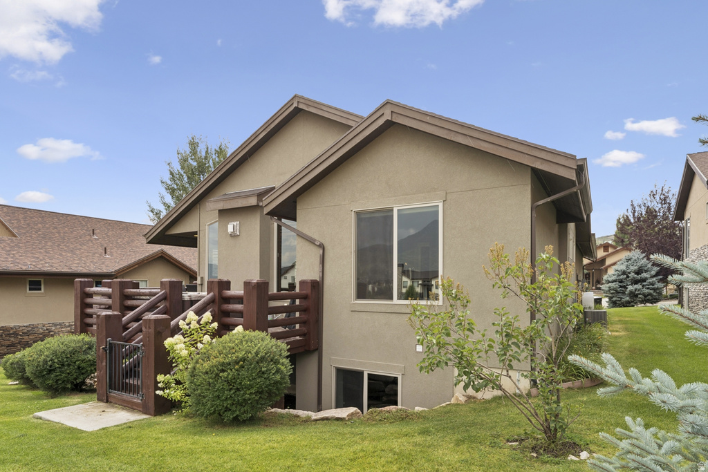 Back of house with stucco siding, a lawn, and a wooden deck