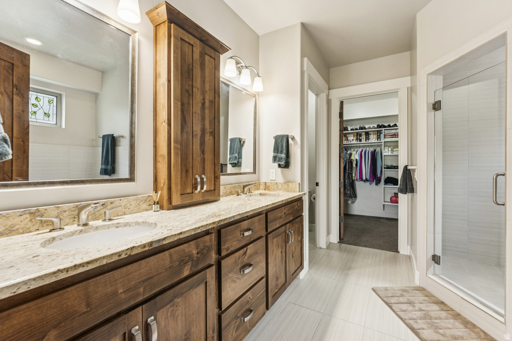 Full bathroom with double vanity, a spacious closet, a stall shower, and light tile patterned flooring