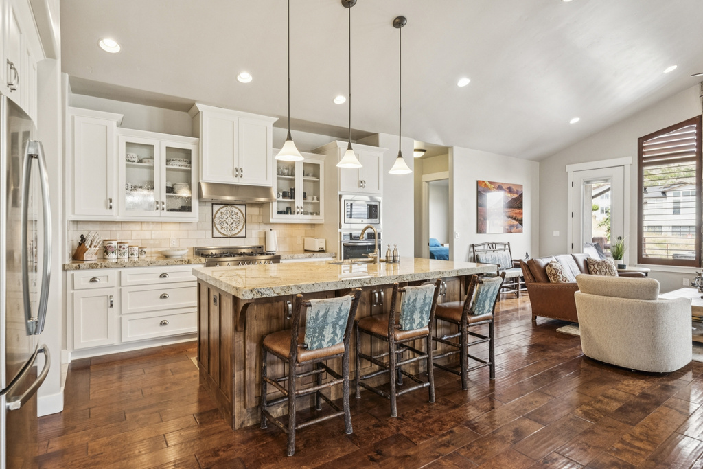 Two tone kitchen with glass fronted cabinets, a breakfast bar area, stainless steel appliances, a kitchen island with sink, and vaulted ceiling