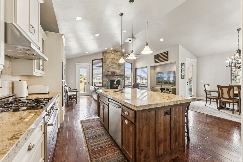 Dual tone kitchen with dark wood-style floors, stainless steel appliances, light stone counters, open floor plan, and two tone cabinetry