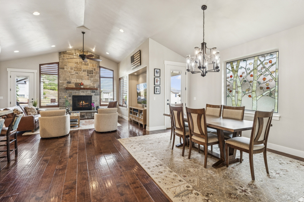Dining area with dark wood finished floors, a stone fireplace, suspended lighting, and a ceiling fan