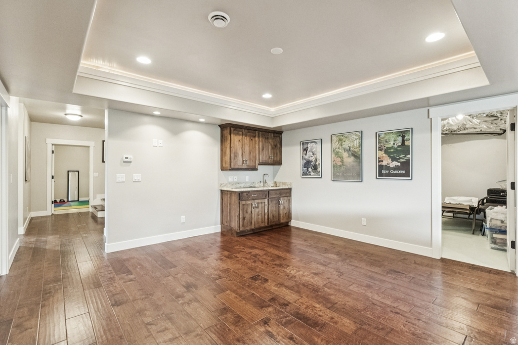 Indoor wet bar featuring a tray ceiling, recessed lighting, dark wood-type flooring, dark wood finish cabinetry, and light stone countertops