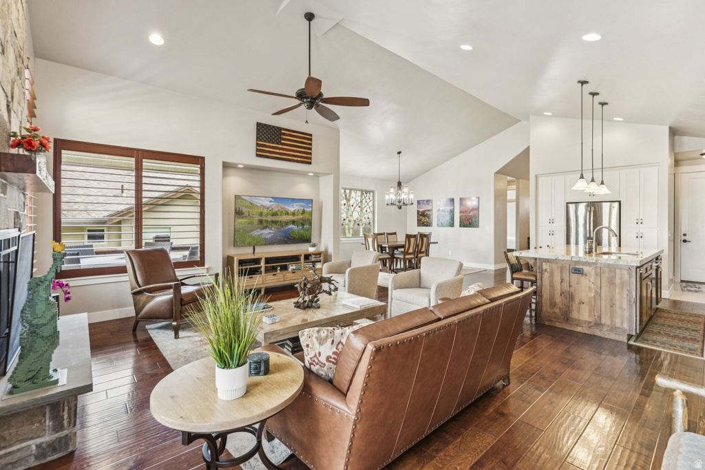 Living room with dark wood-type flooring, ceiling fan, a fireplace with raised hearth, lofted ceiling, and hanging lights