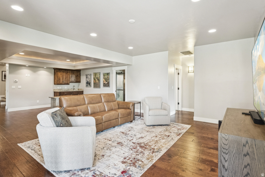 Living area with recessed lighting, a raised ceiling, wet bar, and dark wood-style floors