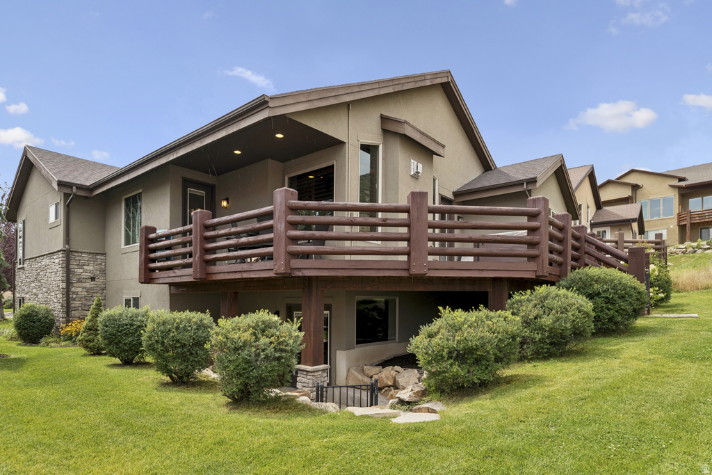 Rear view of house with stucco siding, stone siding, a lawn, a deck, and a patio area