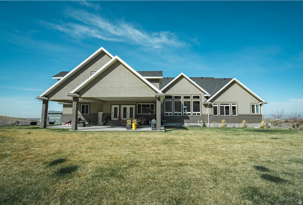 Rear view of property featuring a lawn, a patio, stucco siding, brick siding, and french doors