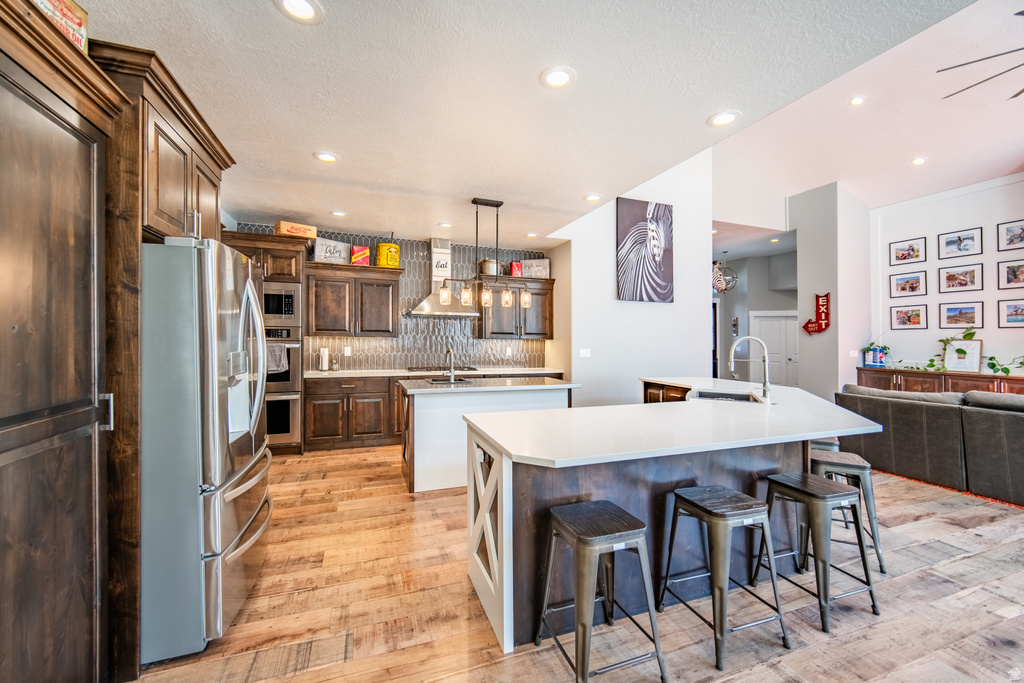 Kitchen with stainless steel appliances, a kitchen breakfast bar, open floor plan, light wood-type flooring, and light stone countertops
