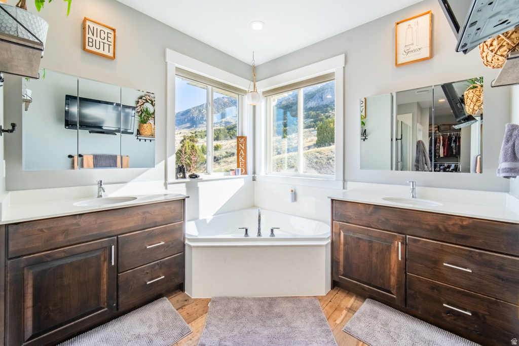 Full bath with a bath, two vanities, and light wood-style flooring