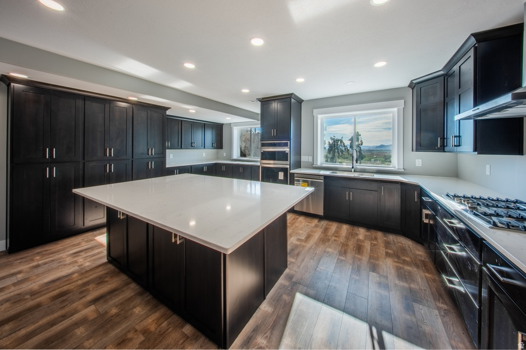 Kitchen with a center island, dark wood-style floors, light stone countertops, stainless steel appliances, and ventilation hood