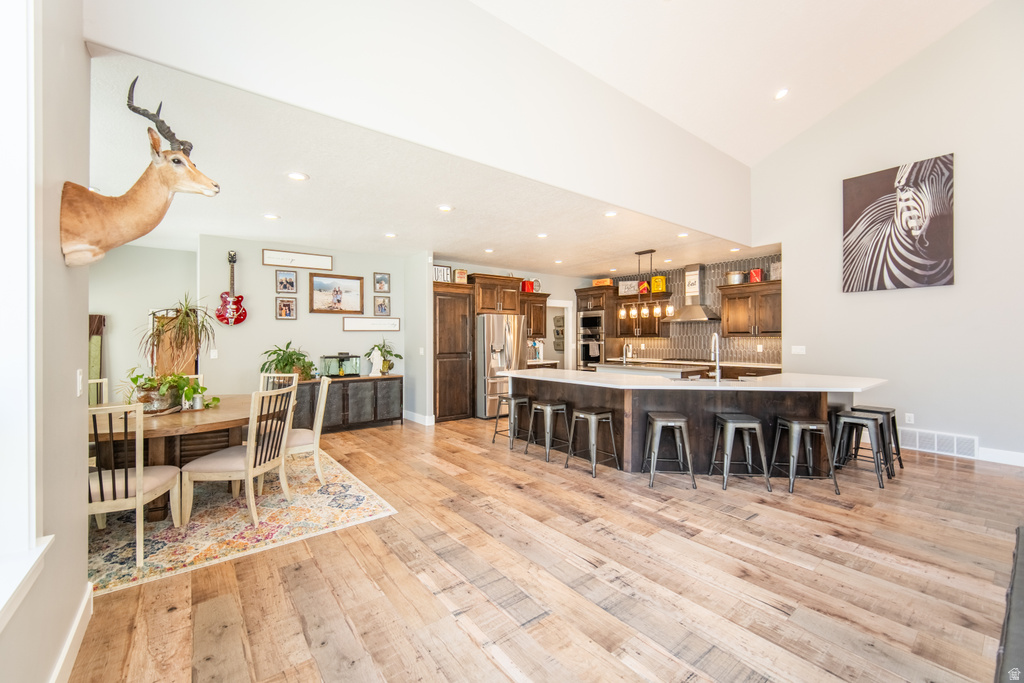 Kitchen with a kitchen breakfast bar, stainless steel fridge with ice dispenser, light wood finished floors, backsplash, and pendant lighting