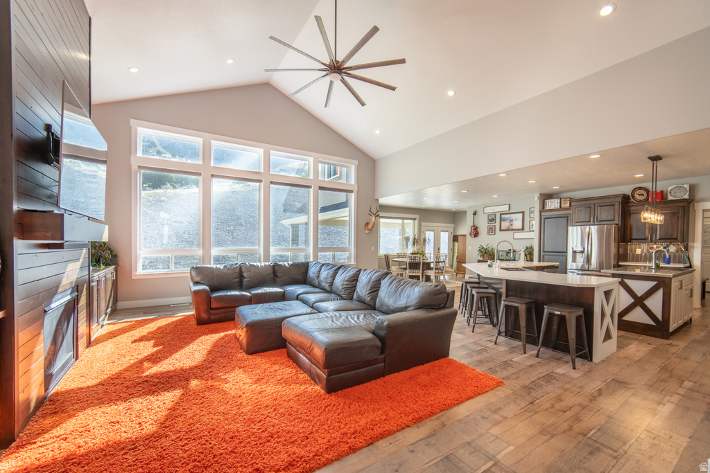 Living room featuring a ceiling fan, a fireplace, light wood finished floors, recessed lighting, and a high ceiling