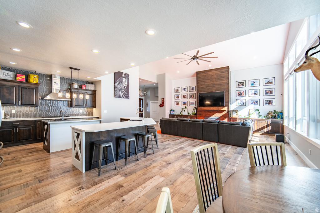 Kitchen featuring open floor plan, dark wood finish cabinetry, backsplash, a kitchen breakfast bar, and light wood finished floors
